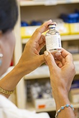 A female pharmacist is examining a vial in a pharmacy.